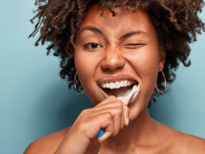 mulher negra escovando os dentes e piscando com o olho esquerdo